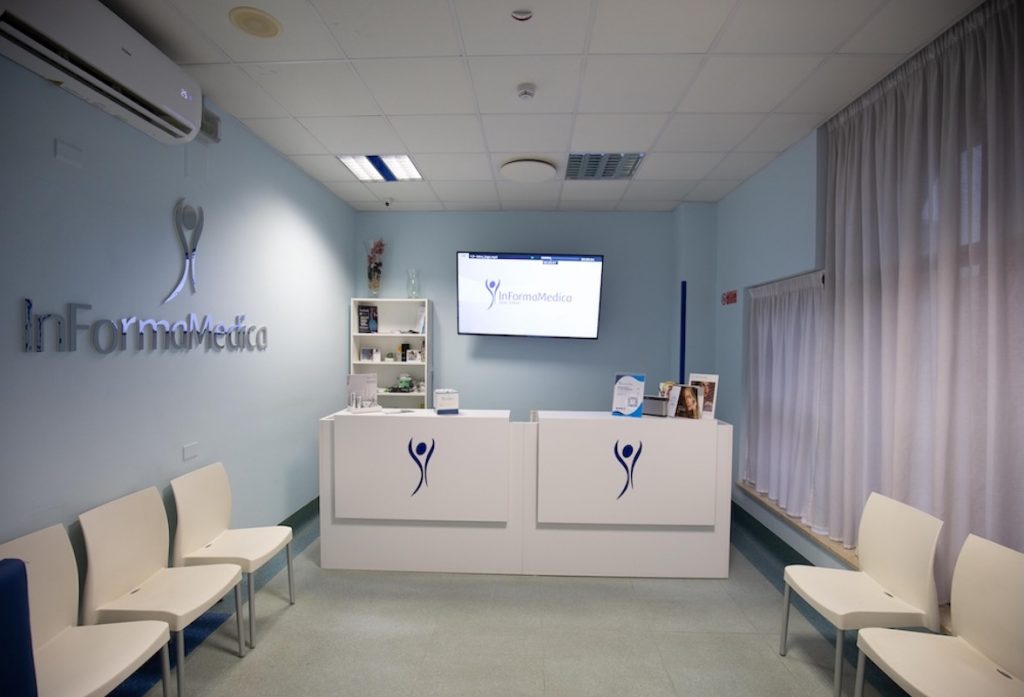 Sala d'aspetto di una clinica medica con sedie, bancone d'accoglienza con logo InFormaMedica